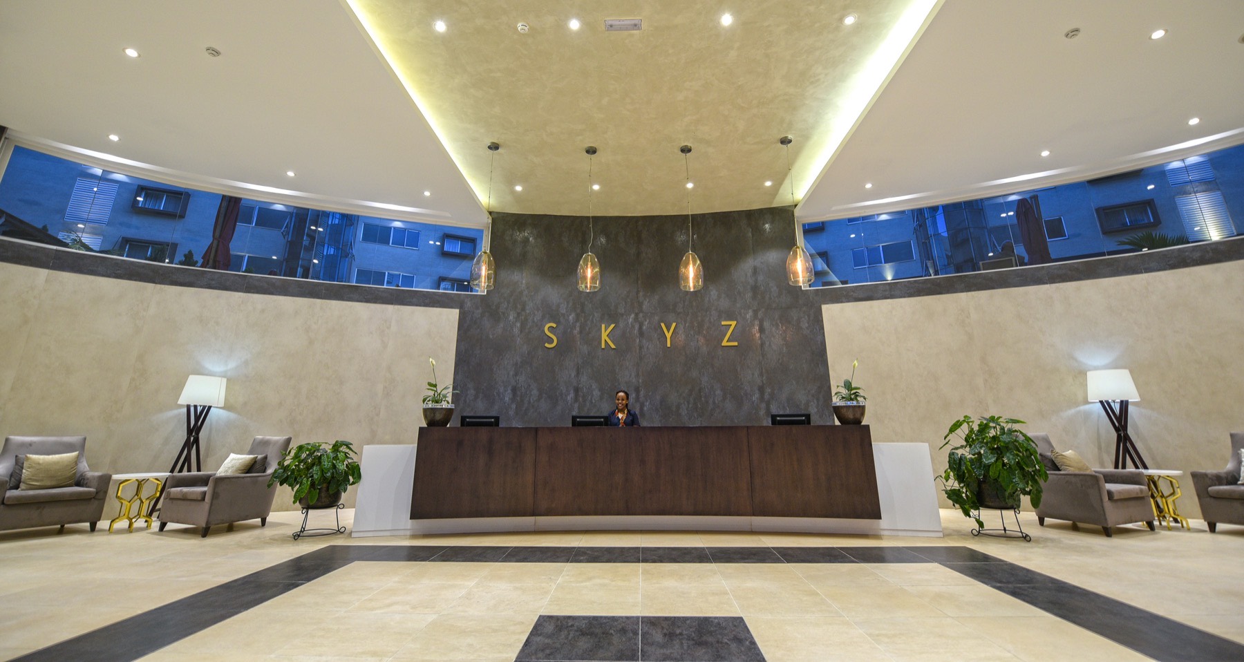 The marble arrival lobby and reception of Skyz Hotel Kampala, with gold SKYZ lettering on the wall behind the desk