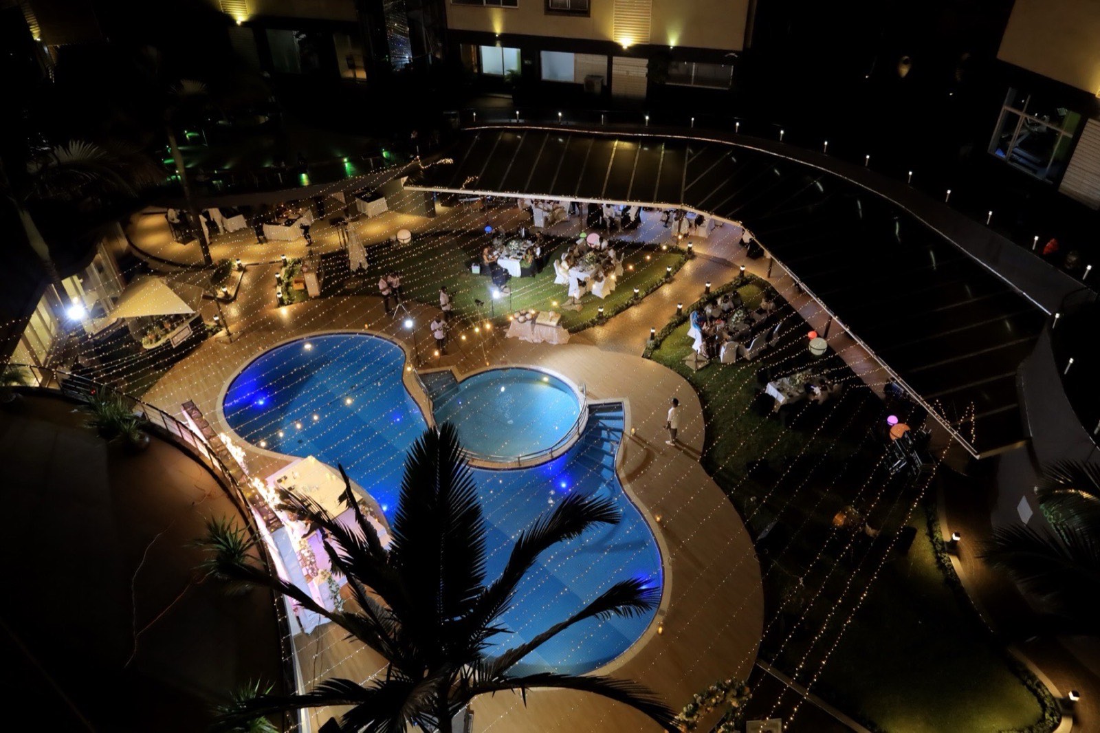 Aerial view of a wedding reception lit with string lights beside the Tropicanna Poolside at night